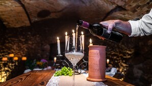 A bottle of wine being poured into a glass, with candles and a rustic setting.