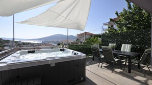 Un jacuzzi en una terraza exterior con una mesa y sillas, con vistas a una ciudad y montañas.