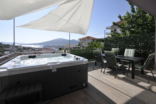 A hot tub on an outdoor deck with a table and chairs, overlooking a city and mountains.