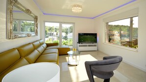 Una sala de estar moderna con un sofá, un televisor y un ventanal que ofrece vistas a zonas verdes y edificios.