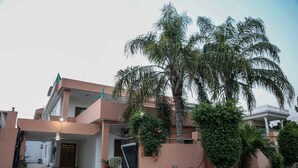 A two-story residential building with a gated entrance, a balcony, and a well-maintained garden with palm trees. - Swiss Cottage (Islamabad)