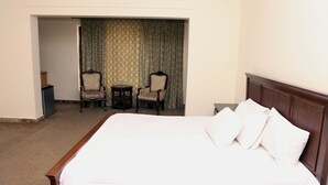 A hotel room with a large bed, two armchairs, a small table, and a door leading to a balcony. - Swiss Cottage (Islamabad)