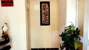 A hallway with a tiled floor, a potted plant, and a wall-mounted sign with Arabic calligraphy. - Swiss Cottage (Islamabad)