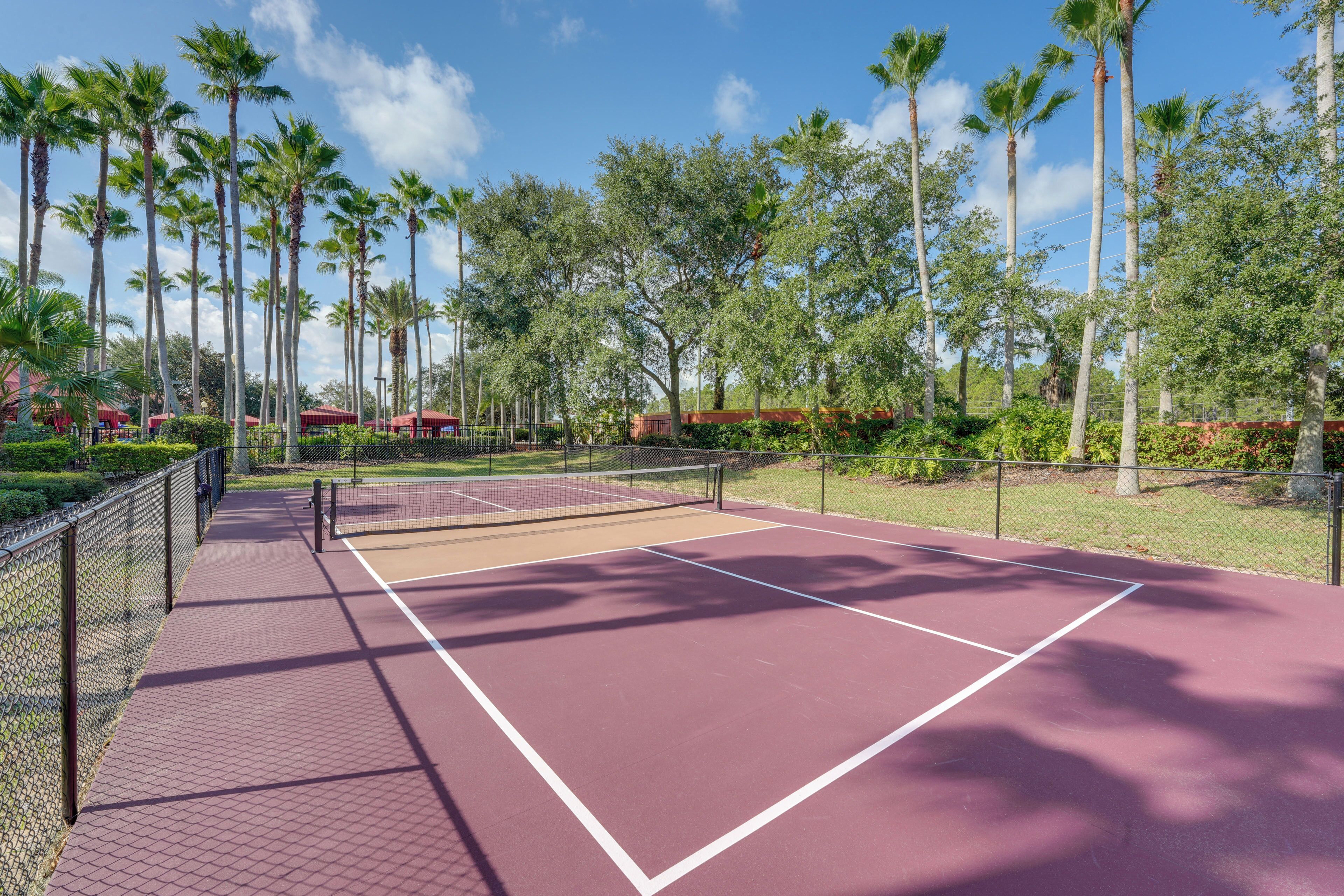 A tennis court with a net, surrounded by palm trees and a fence.