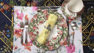 Une table dressée avec une nappe à motifs floraux, un porte-serviette, des couverts et une tasse avec sa soucoupe.