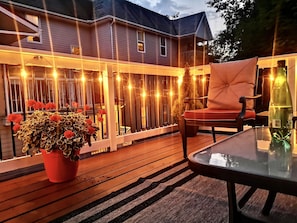 A wooden deck with string lights, a potted plant with red flowers, and a glass table.