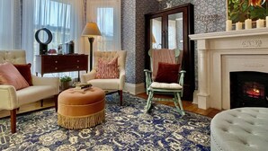 A living room with a fireplace, a patterned rug, a sofa, a chair, and a lamp. - Charlotte's Rose Inn (Charlottetown)