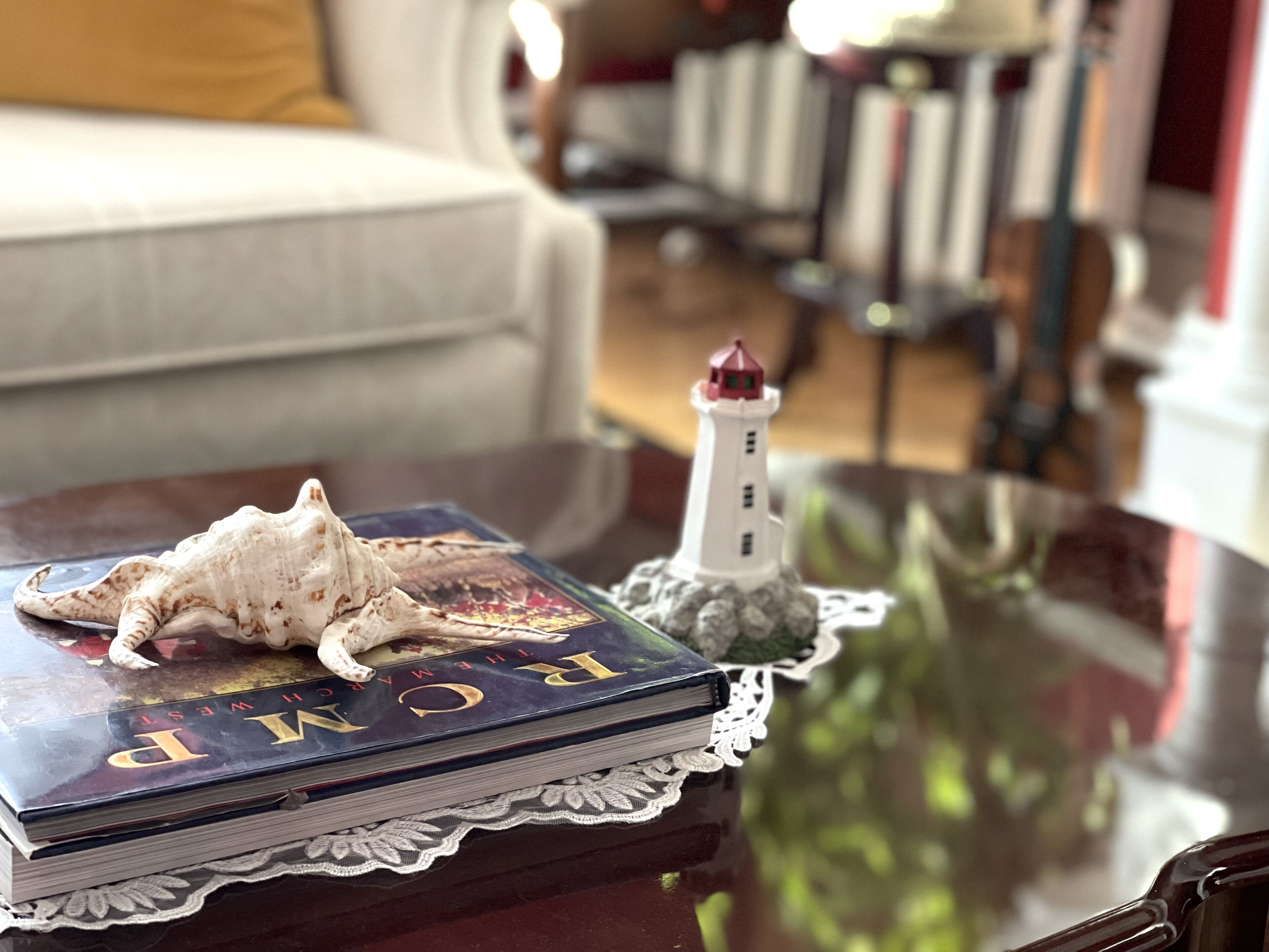 A book titled "The World" on a glass table with a lace doily, a small lighthouse model, and a seashell.
