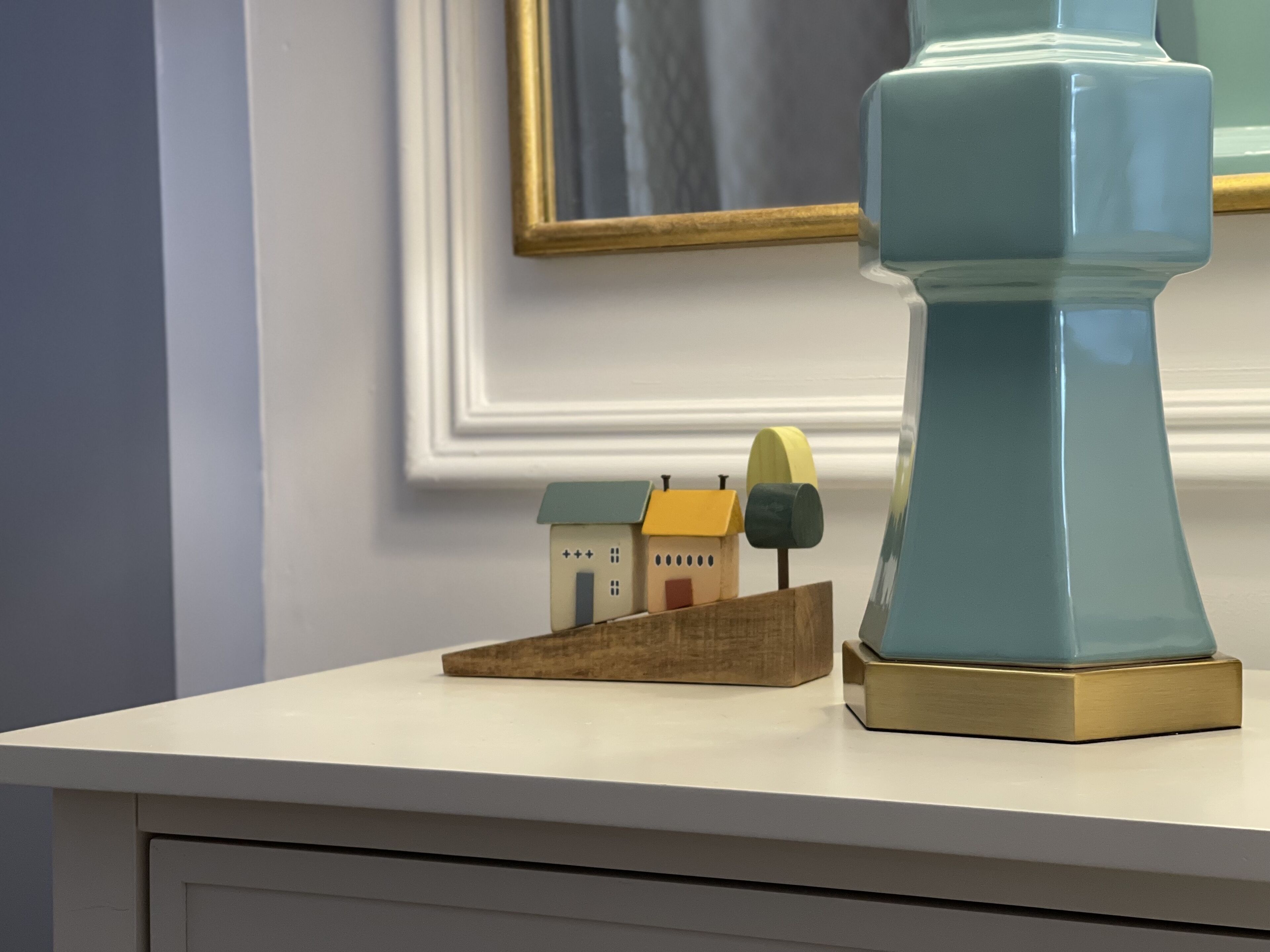 A white table with a blue object on top, a small wooden house model, and a framed picture on the wall.