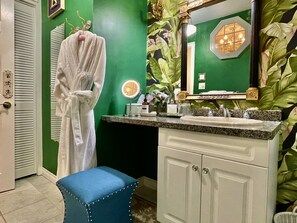 A bathroom with a green wall, a white vanity with a mirror, a sink, and a blue stool. - Charlotte's Rose Inn (Charlottetown)