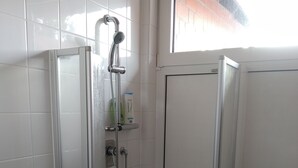 Lasiseinöillä varustettu suihkutila, jossa on käsisuihku, wc-paperiteline ja pieni hylly hygieniatuotteille.