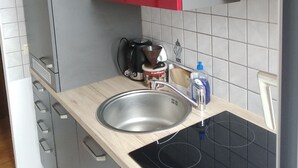 Keittiössä on ruostumattomasta teräksestä valmistettu pesuallas, kahvinkeitin ja punainen yläkaappi työtason yläpuolella.
