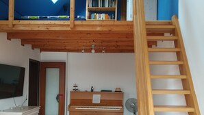 Avoin, parvimainen makuuhuone, jossa on puinen portaikko, piano, televisio ja kirjahylly.