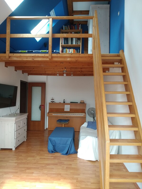 A loft-style bedroom with a wooden staircase, a piano, a television, and a bookshelf. - Sunny studio oasis (Göttingen)