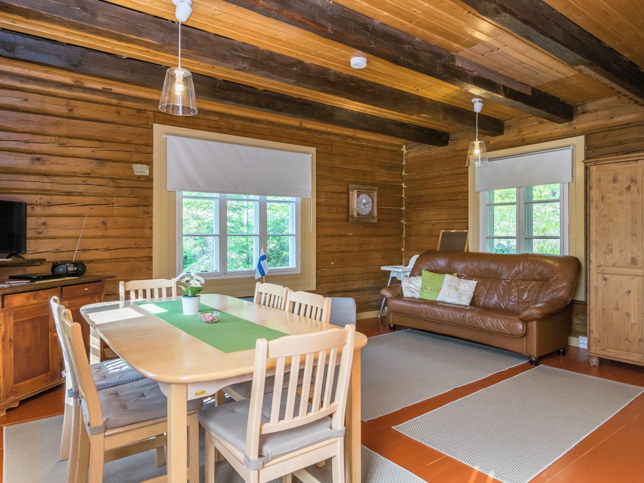 A wooden interior with a dining table, chairs, a sofa, and a television.