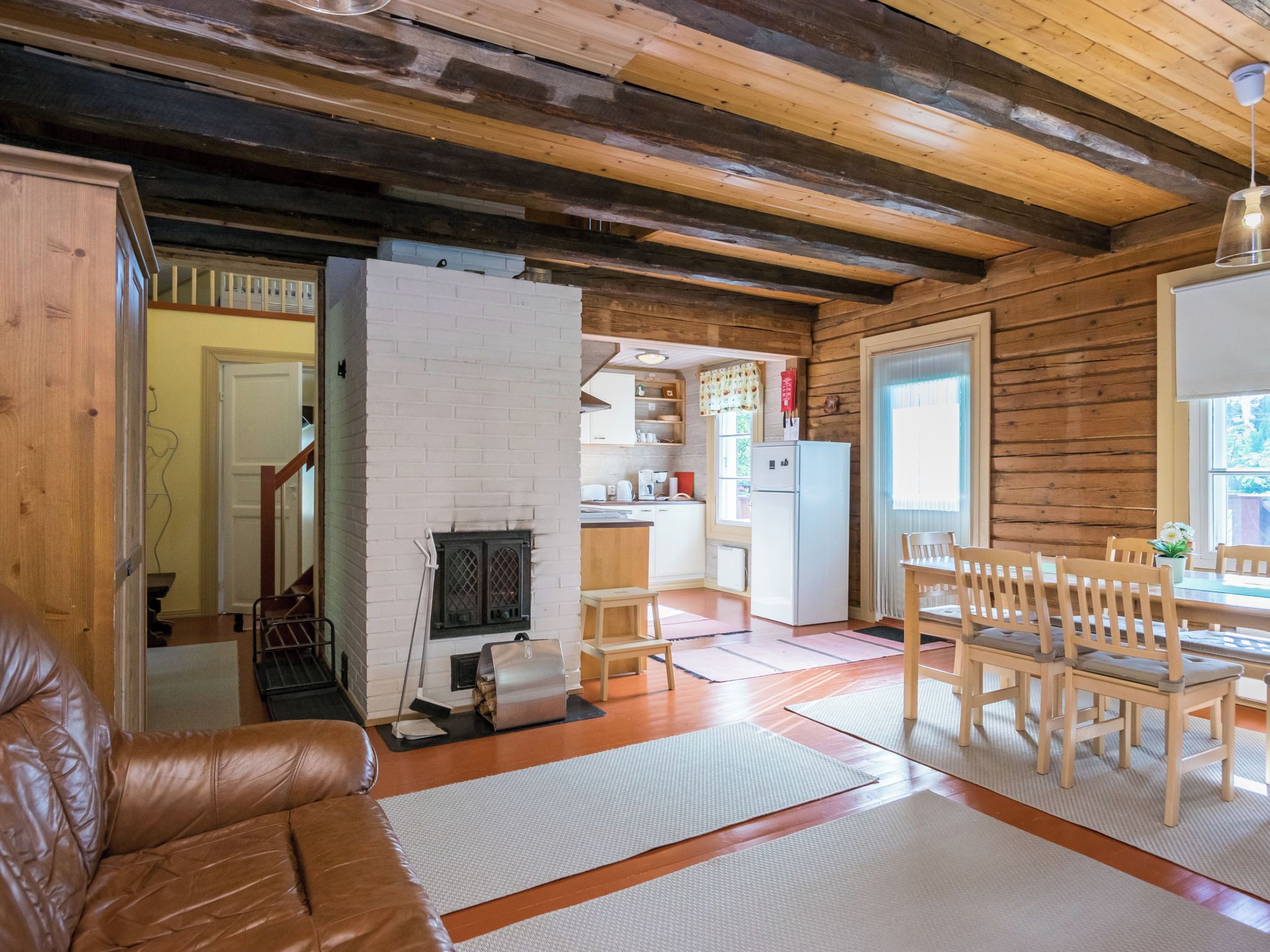 Un salon chaleureux avec un canapé en cuir, une cheminée et un coin repas comprenant des chaises et une table en bois.