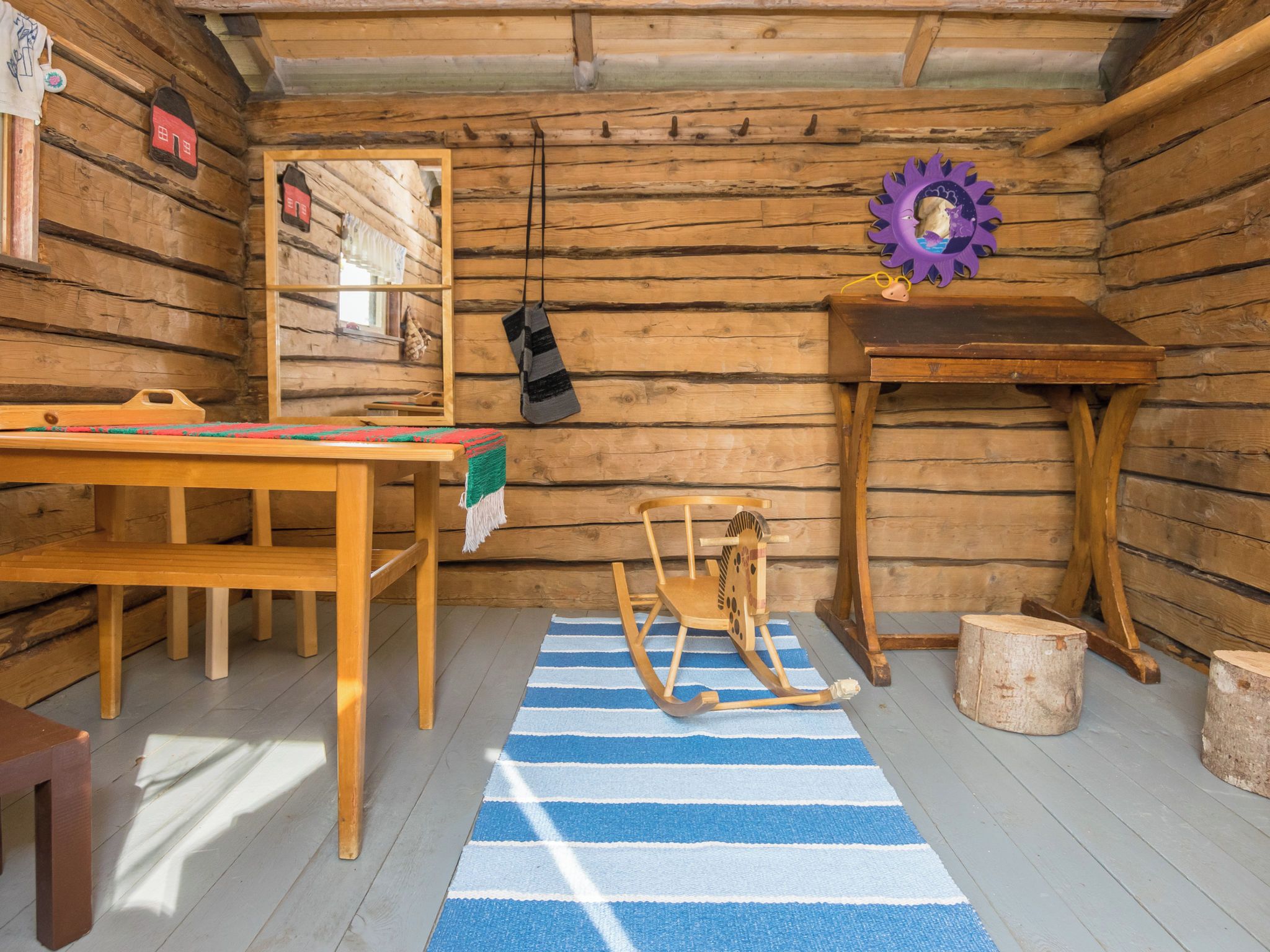 L’intérieur d’un chalet rustique en bois, avec une table en bois, un fauteuil à bascule et un petit tabouret en bois.