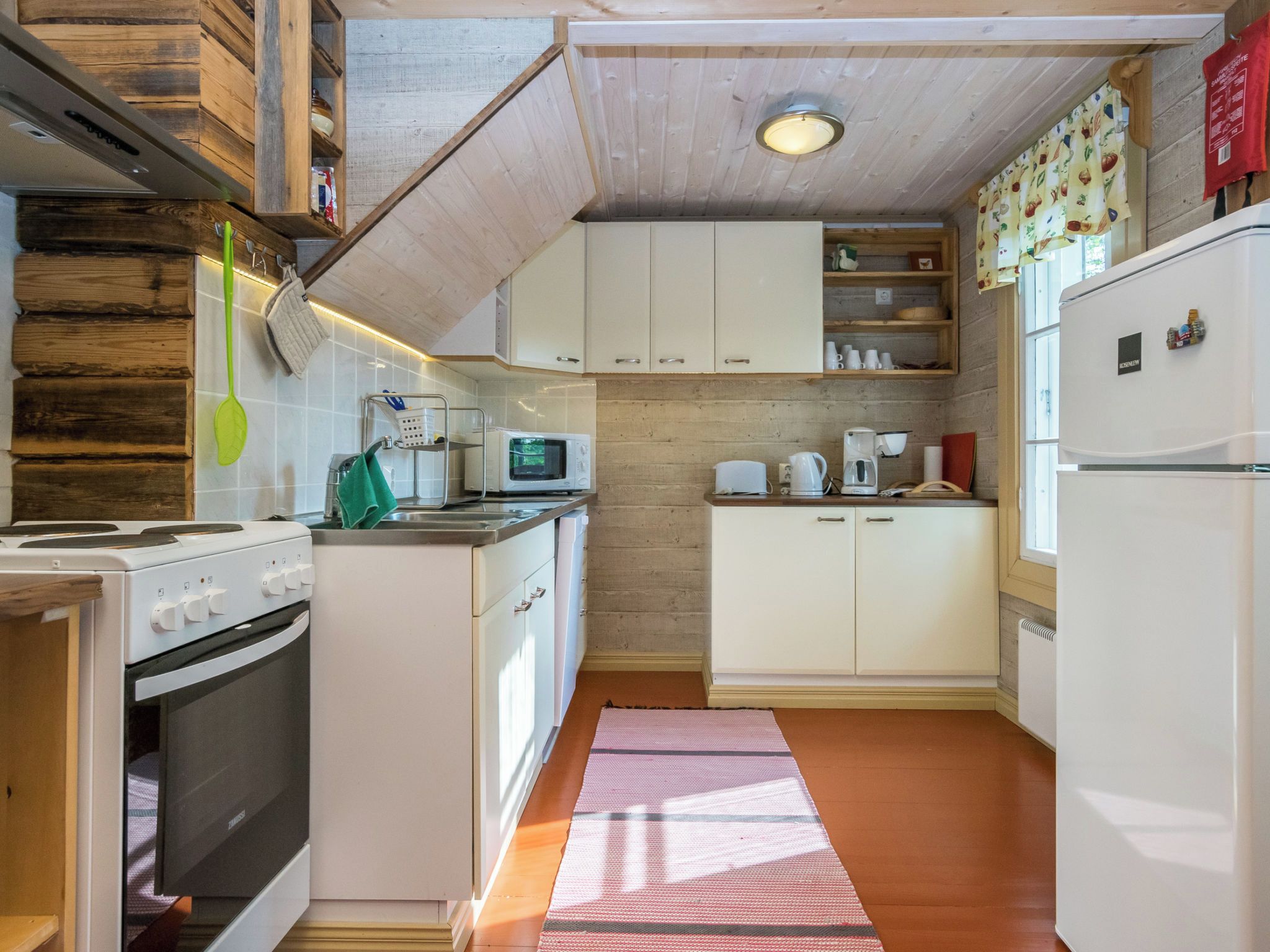 Una cucina compatta con mobili bianchi, un forno a microonde, un bollitore e un frigorifero.