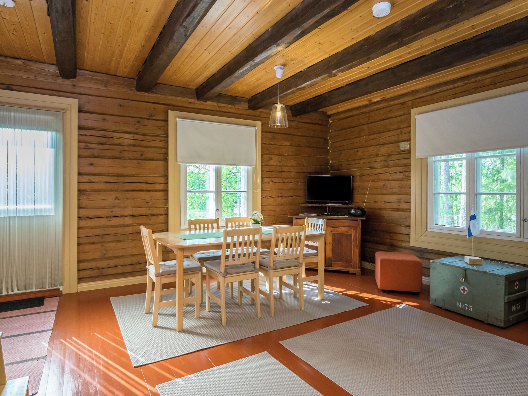 Un interno di una baita in legno con un tavolo da pranzo, sedie, un televisore e un piccolo kit di pronto soccorso.