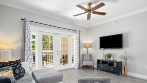 A living room with a grey sofa, a grey armchair, a black TV stand, and a ceiling fan. - Beautiful Condo Near Amenities and Attractions (Kissimmee)