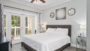A bedroom with a large bed, a ceiling fan, a nightstand with a lamp, and a view of the outdoors through a glass door. - Beautiful Condo Near Amenities and Attractions (Kissimmee)