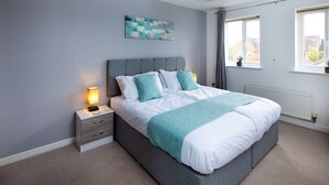 Un dormitorio moderno con una cama tapizada en gris, ropa de cama blanca y detalles en verde azulado.
