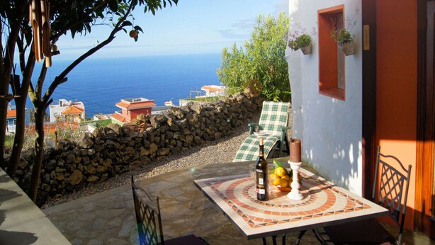 Une terrasse avec une table dressée pour deux personnes, une bouteille de vin et une bougie. La table est située à l’extérieur et offre une vue sur la mer.