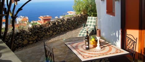 Une terrasse avec une table dressée pour deux personnes, une bouteille de vin et une bougie. La table est située à l’extérieur et offre une vue sur la mer.