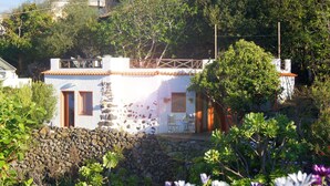 Un bâtiment blanc avec un mur en pierre, une clôture en bois et une terrasse aménagée avec du mobilier d’extérieur.