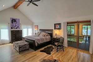 Relax in this serene bedroom with a large bed, wooden floor, and a view of lush greenery.