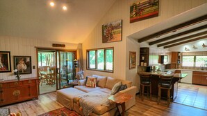A spacious living room with a sofa, a coffee table, and a rug. There is a dining area with chairs and a kitchen in the background.