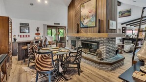 A spacious living room with a fireplace, wooden walls, and a dining area with zebra-striped chairs.