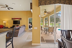 Relax in this open-plan living area with a sofa, dining table, and flat-screen TV, leading to a patio with pool and outdoor seating.