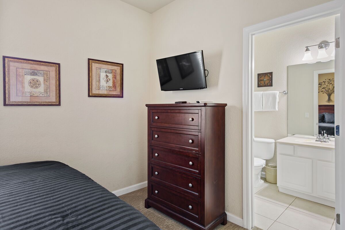 A bedroom with a bed, a dresser, a television, and a bathroom with a sink and toilet.