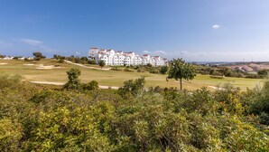 Un edificio grande y blanco de varios pisos con techos rojos, rodeado por un campo de golf bien cuidado y vegetación.