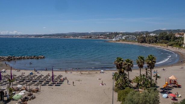 Una playa con sombrillas, palmeras y un parque infantil.