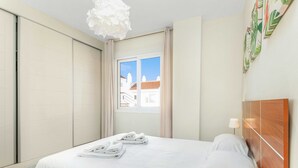 Habitación de hotel con una cama, ventana con cortinas y vistas a edificios, además de una pared decorada con una planta.