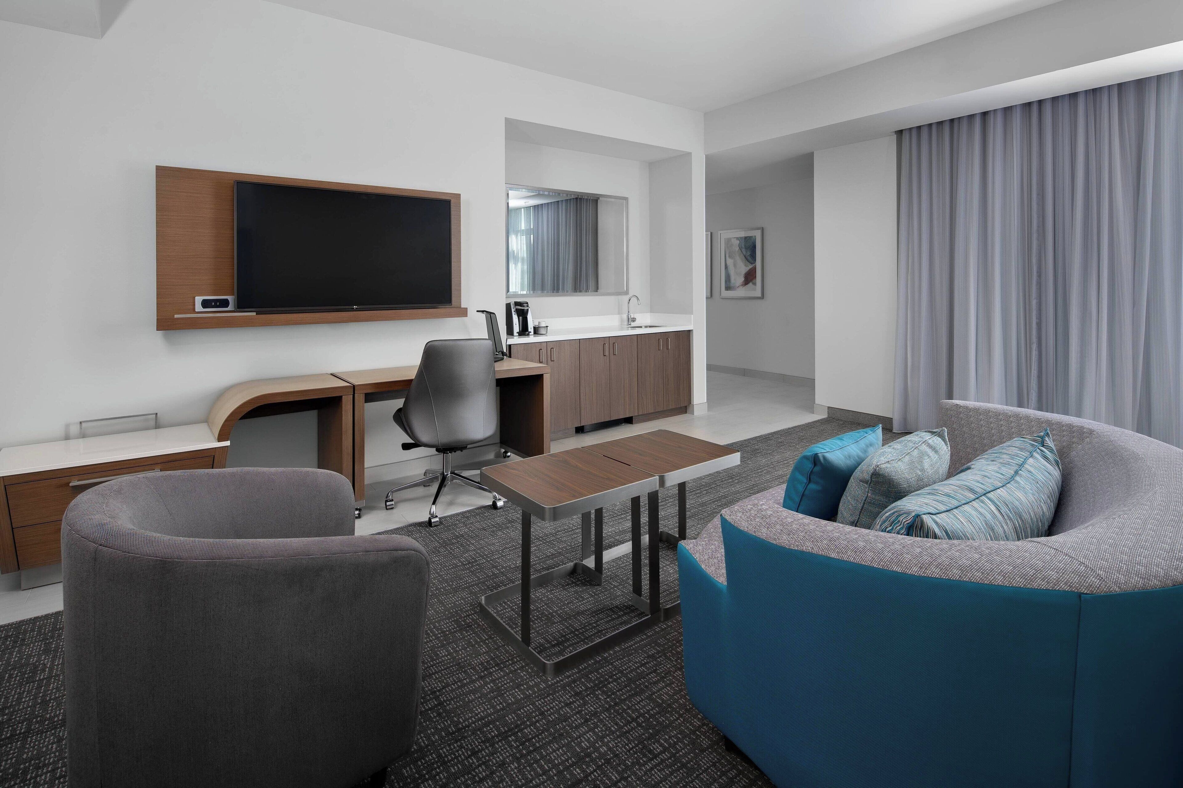 Habitación de hotel moderna con televisor de pantalla plana, escritorio, sofá y kitchenette.