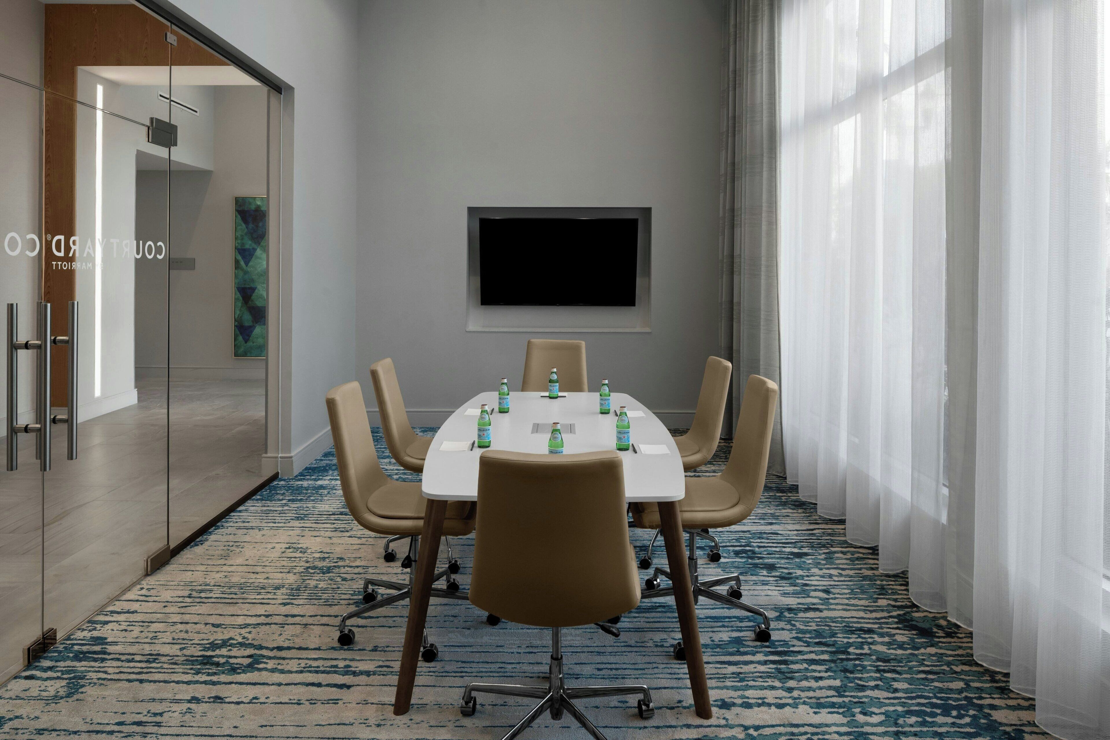 A conference room with a white table, six chairs, and a flat-screen TV on the wall.