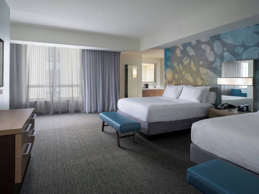 A hotel room with a large bed, a desk, a bench, and a bathroom visible through a door.