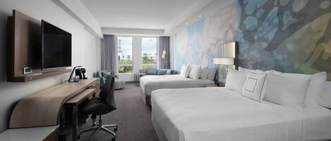 Une chambre d’hôtel équipée d’une télévision à écran plat, d’un bureau avec une chaise, de deux lits et d’une grande fenêtre donnant sur des immeubles.