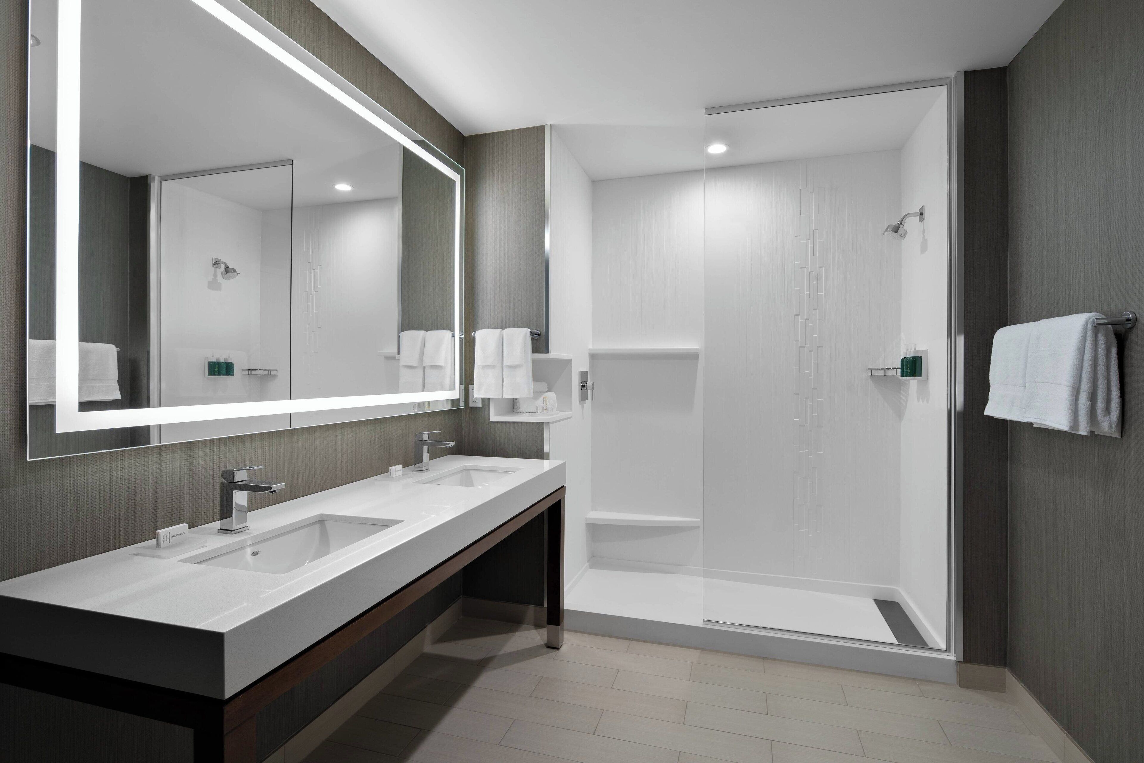 A modern bathroom with two sinks, a large mirror, and a glass-enclosed shower.