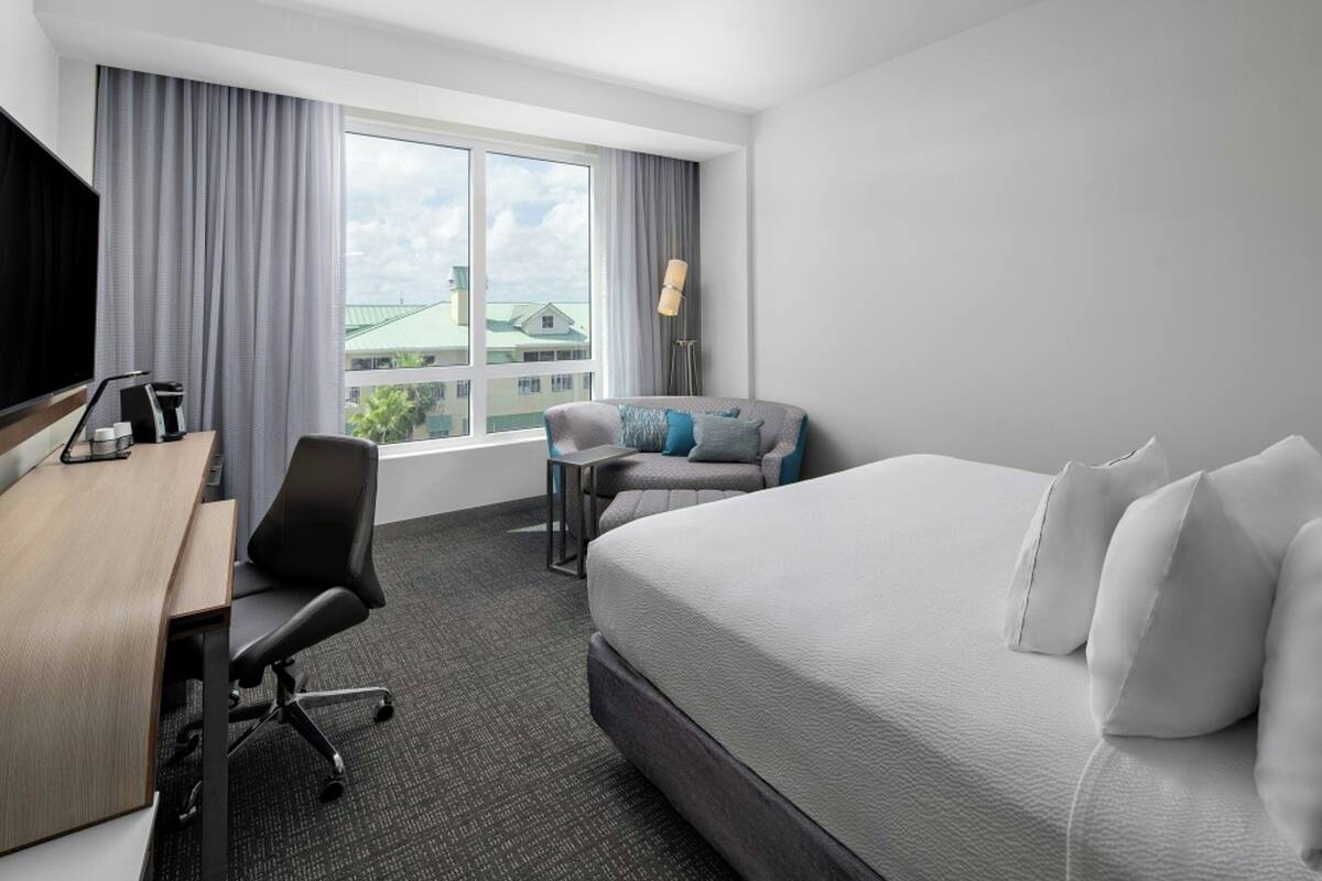 A hotel room with a bed, a desk, a chair, and a TV.