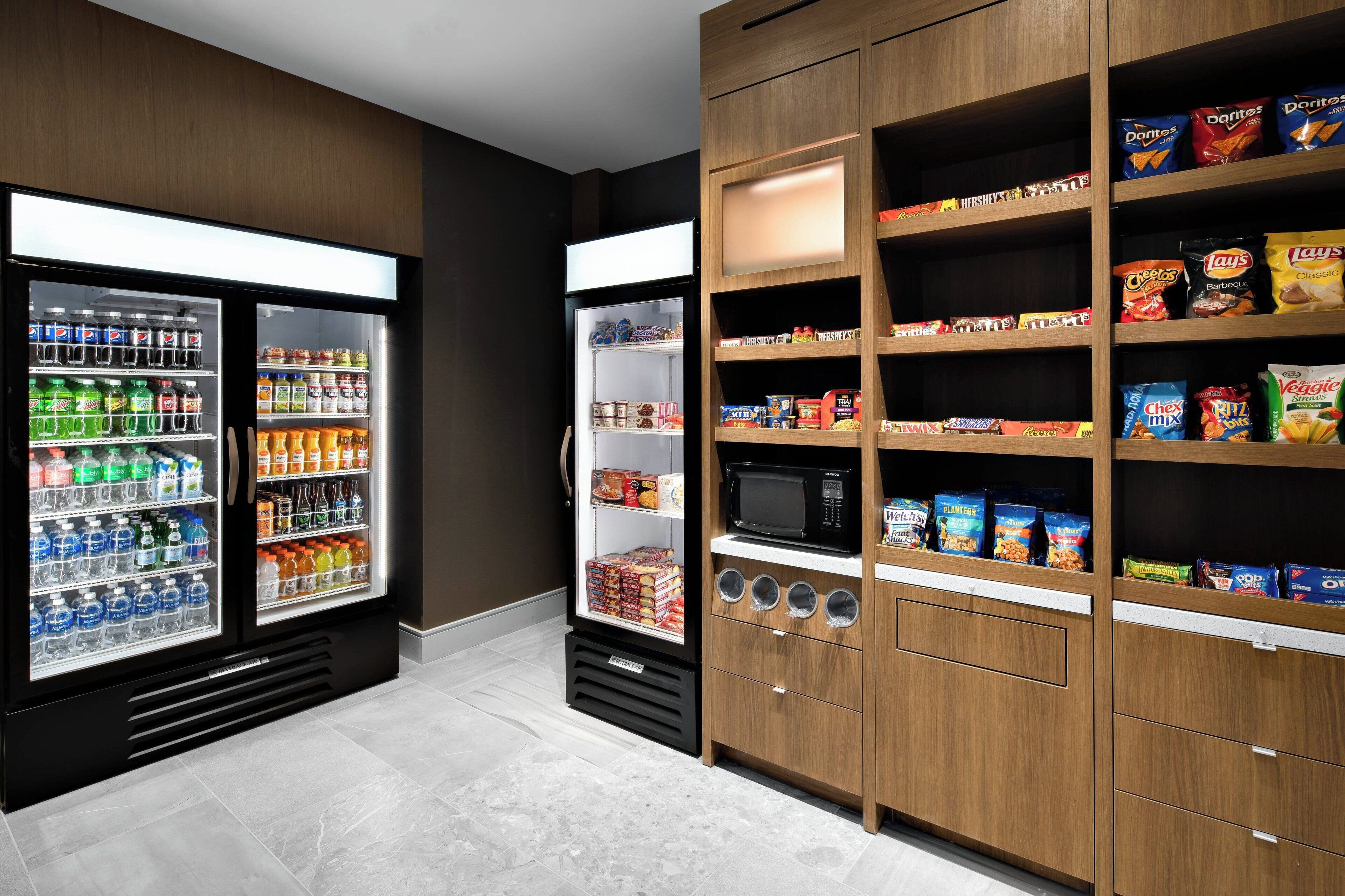 A self-service snack and beverage area with refrigerated drink dispensers and shelves stocked with snacks and chips.