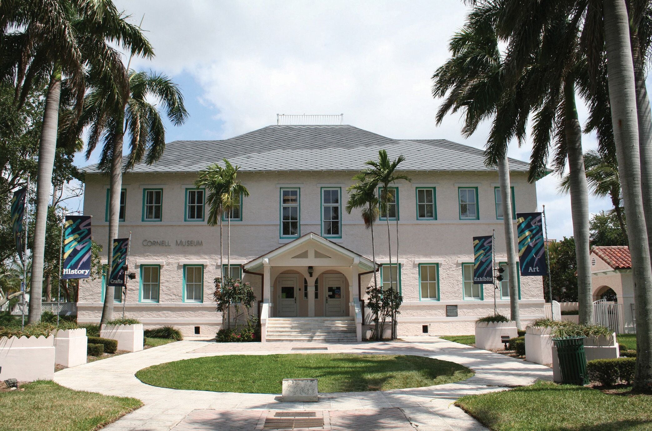 A two-story building with a symmetrical facade, a central entrance with a covered porch, and palm trees surrounding the property.