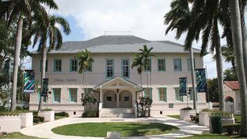 A two-story building with a symmetrical facade, a central entrance with a covered porch, and palm trees surrounding the property.
