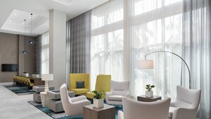 A modern hotel lobby with a seating area, large windows, and a flat-screen TV. - Courtyard by Marriott Delray Beach (Delray Beach)