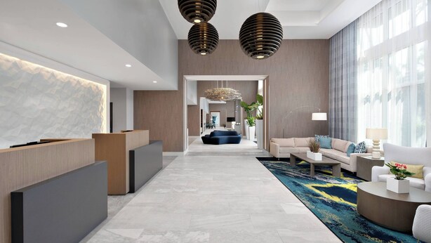 A modern hotel lobby with a reception desk, seating area, and a view into the dining room. - Courtyard by Marriott Delray Beach (Delray Beach)
