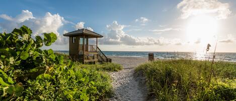 Une cabane en bois située sur la plage, avec un escalier menant à une terrasse d’où l’on a une vue sur l’océan.