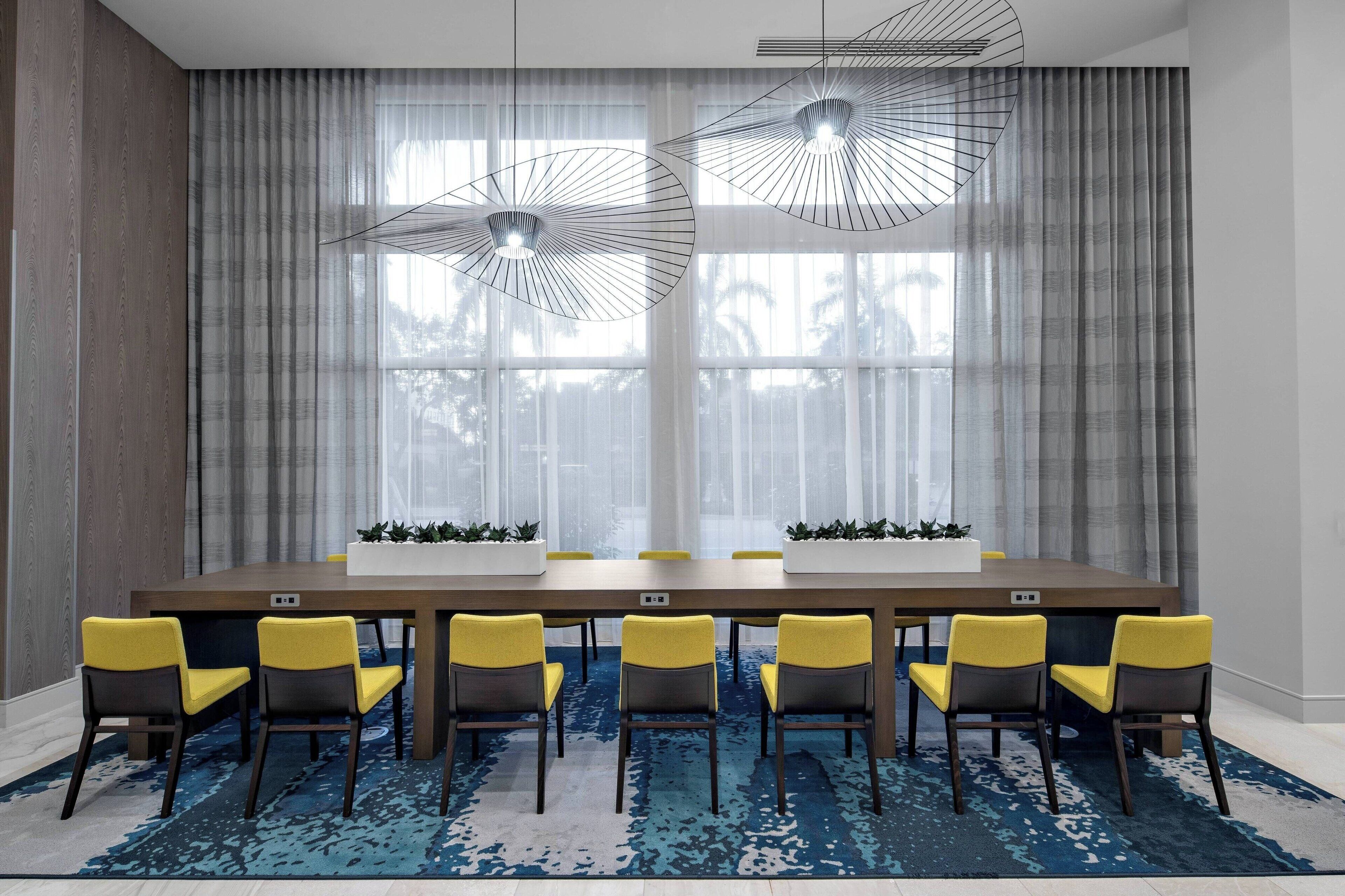 A conference room with a long table, six yellow chairs, and two pendant lights.